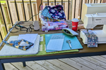 A Baby Lock sewing machine on an outdoor deck table with quilting fabric, cutting mat, scissors, and a Tim Hortons coffee cup