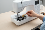 A modern sewing machine with the bobbin cover removed, showing the inside mechanism being cleaned with a lint brush