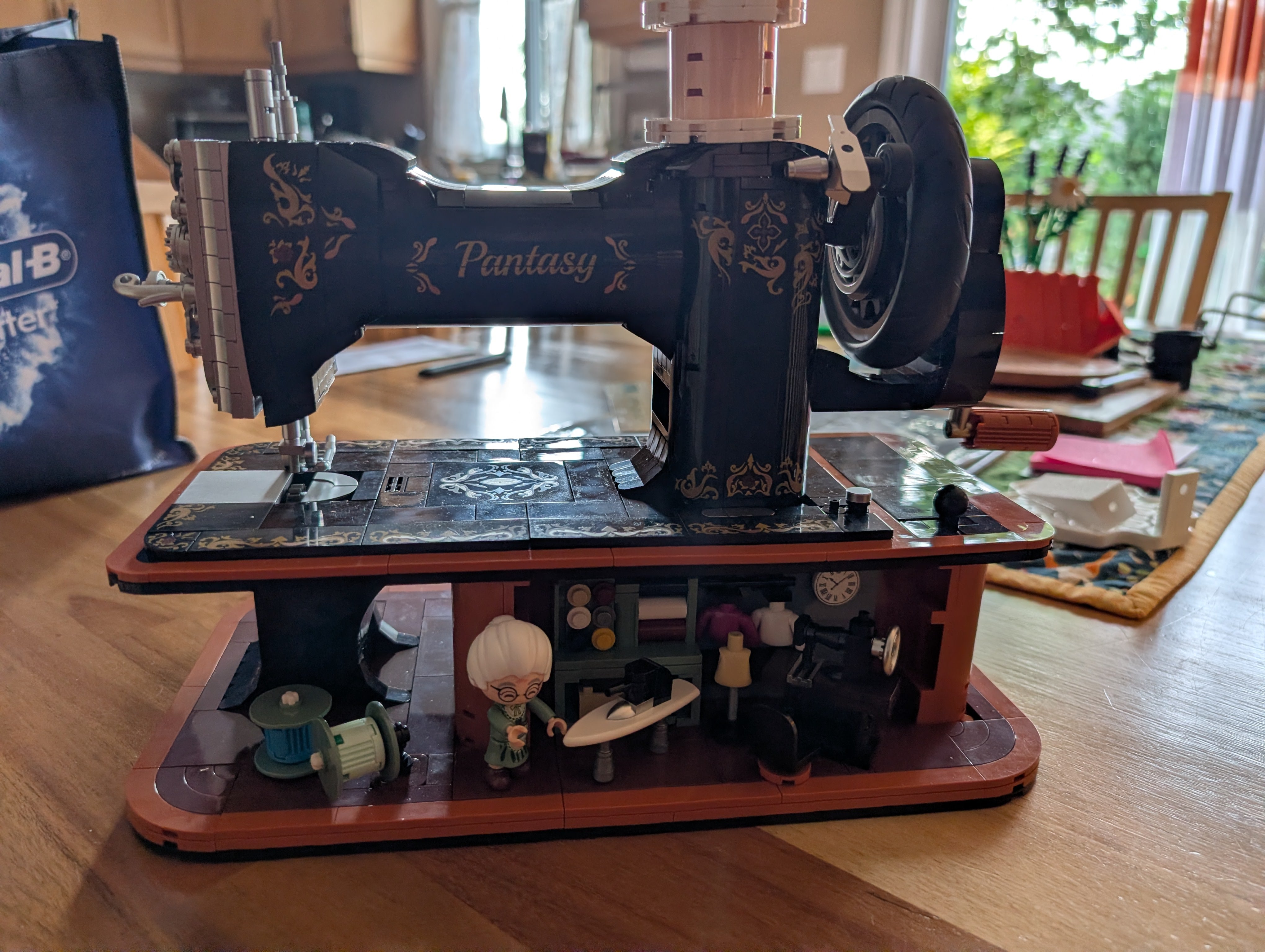 Lego-style building block sewing machine in progress, showing the ornate black and gold machine body with the fabric shop base underneath